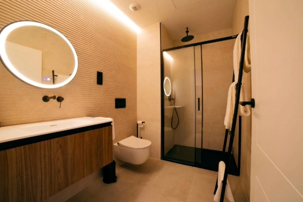 Baño contemporáneo con ducha de cristal, espejo redondo y luz cálida.