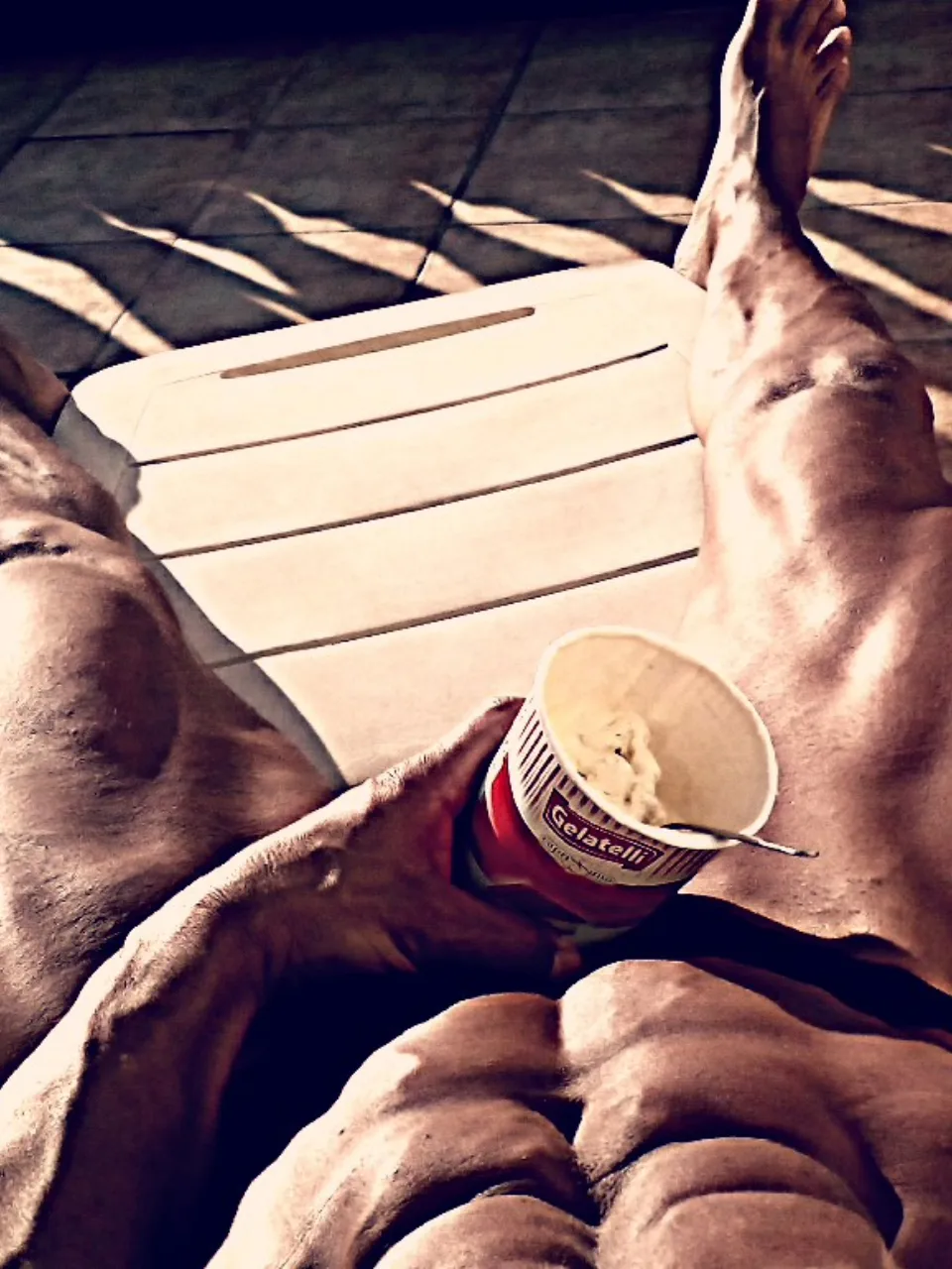 Hombre musculoso descansando al sol en una tumbona mientras sostiene un helado.