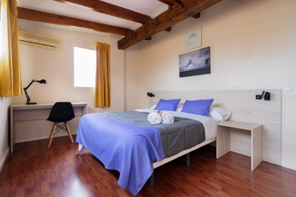 Habitación luminosa con cama doble, escritorio y techo con vigas de madera.