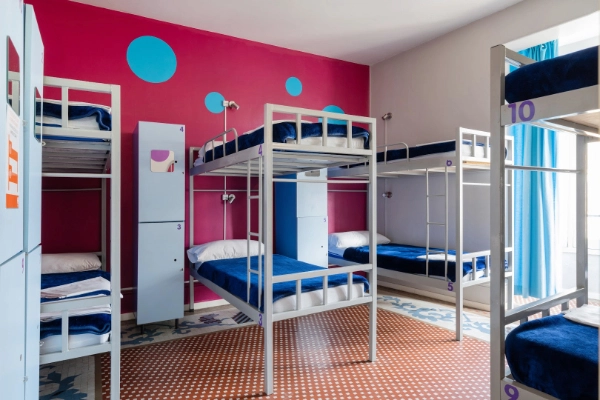 Literas metálicas en habitación con paredes rosas y decoración con círculos.