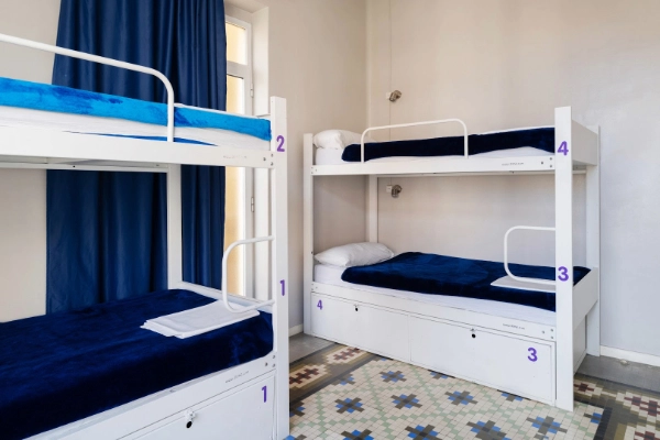 Literas blancas con ropa de cama azul en dormitorio compartido.
