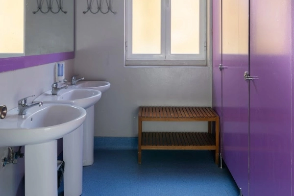 Lavabos dobles, banco de madera y cabinas de baño en zona compartida.