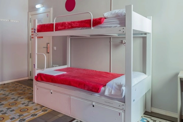 Litera blanca con ropa de cama roja en dormitorio compartido.