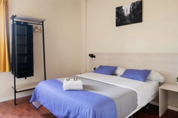 Habitación con cama doble, perchero y decoración minimalista para grupos o parejas.