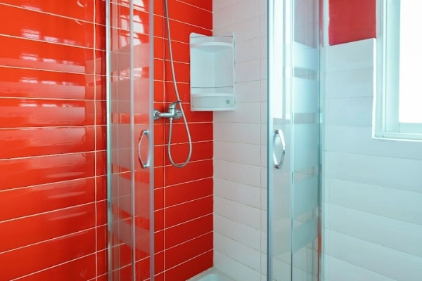 Ducha moderna con azulejos rojos en alojamiento para despedidas en Valencia.