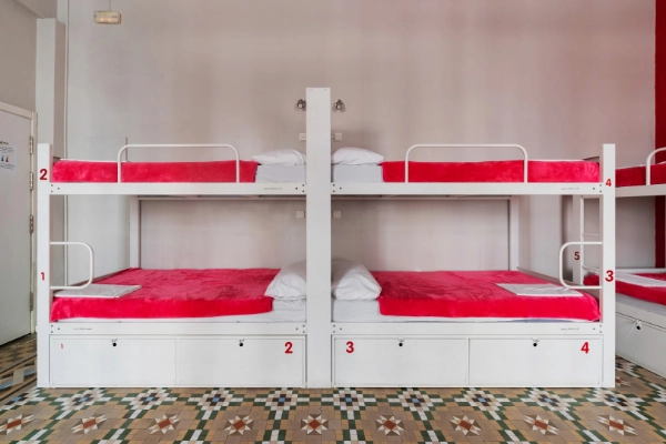 Litera doble con sábanas rojas y suelo hidráulico en habitación del Red Nest Hostel Valencia.