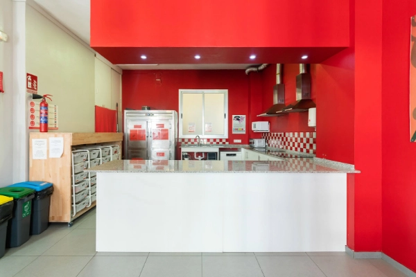 Cocina amplia y equipada del Red Nest Hostel, con mesas para grupos y decoración en rojo.