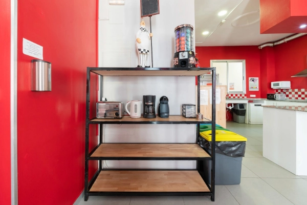 Estantería con cafeteras, utensilios y snacks en cocina común del Red Nest Hostel.