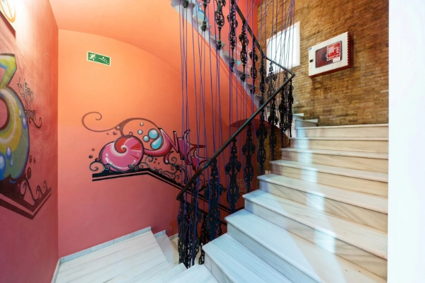 Escaleras principales del Red Nest Hostel con barandilla clásica de forja y decoración moderna.