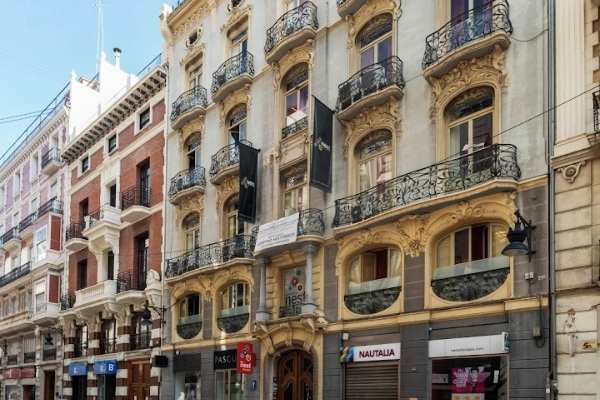 Fachada del Red Nest Hostel en el centro histórico de Valencia, rodeado de tiendas y restaurantes.