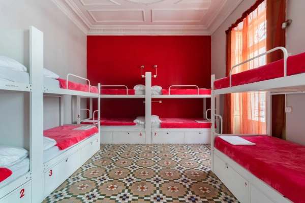 Habitación compartida con literas blancas y ropa de cama roja en el Red Nest Hostel de Valencia.