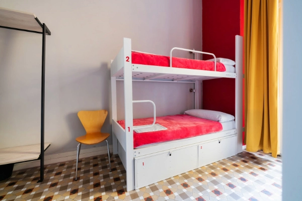 Litera blanca con sábanas rojas en habitación compartida del Red Nest Hostel.