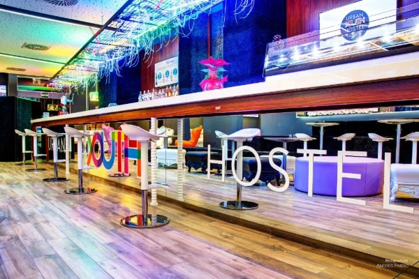Bar moderno del Hostel Urban Youth Valencia con luces LED y logo en cristal.