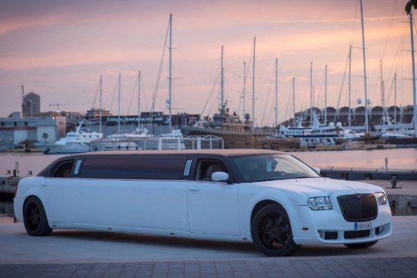 Limusina Chrysler blanca estacionada en la Marina de Valencia al atardecer.